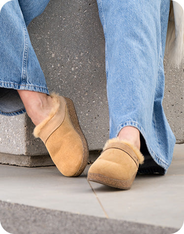 dettaglio donna all'aperto seduta su un cubo di cemento che indossa pantofole con pelo haflinger snowbird beigemeliert